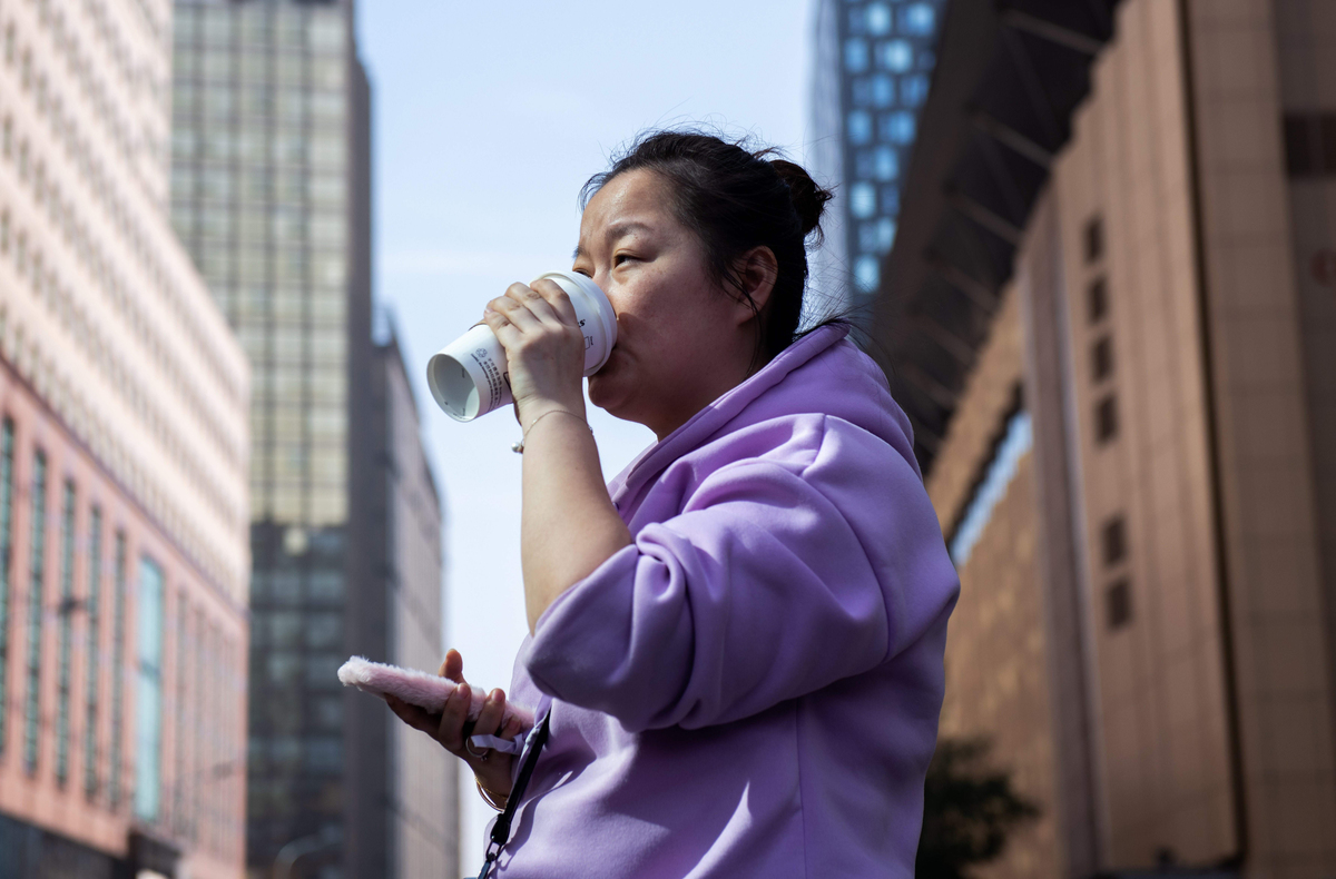 A woman drinks a coffee on a street in Beijing.