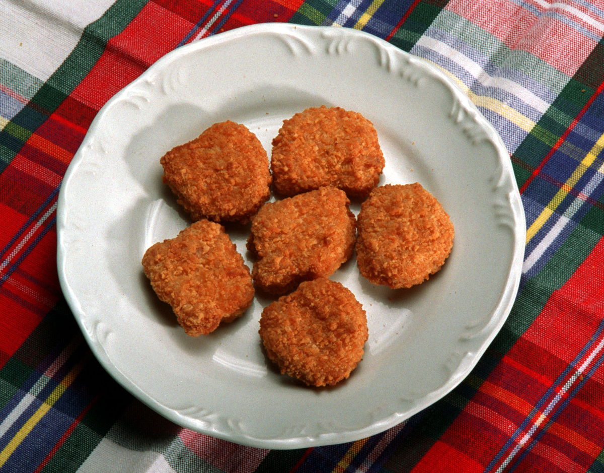 Processed chicken nuggets sit on a plate over a plaid blanket.