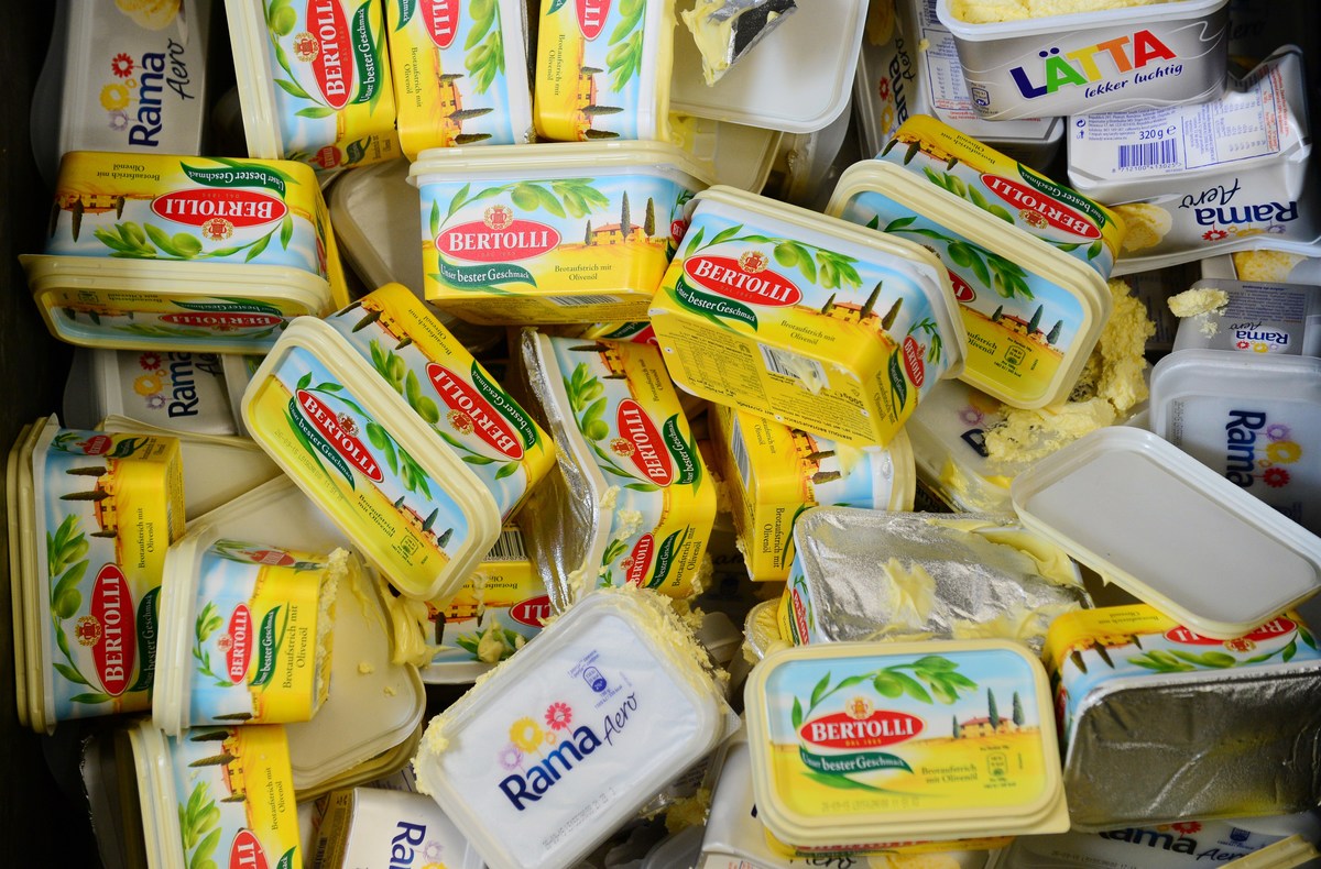 Margarine containers are piled in a trash can.