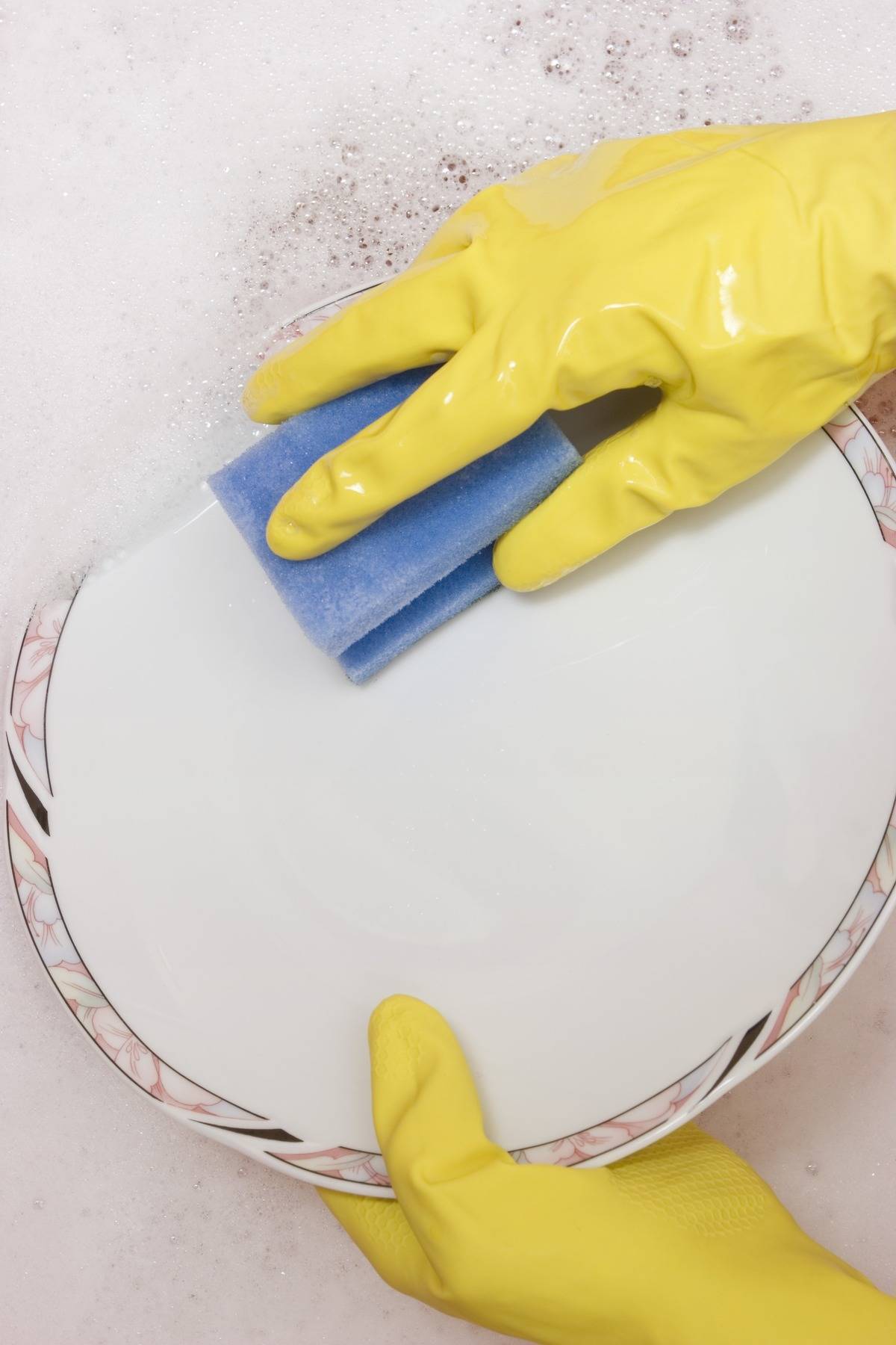 A person wearing gloves washes a dish with a sponge.