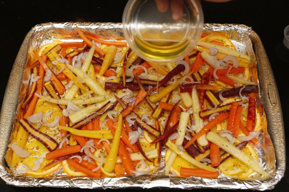 A person pours olive oil onto a pan of carrots to roast.