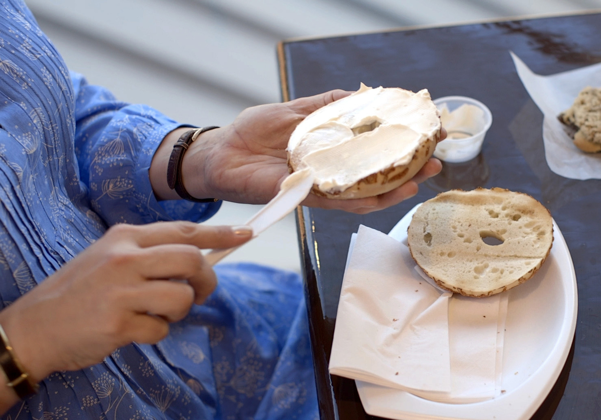 A woman spreads cream cheese on a bagel.