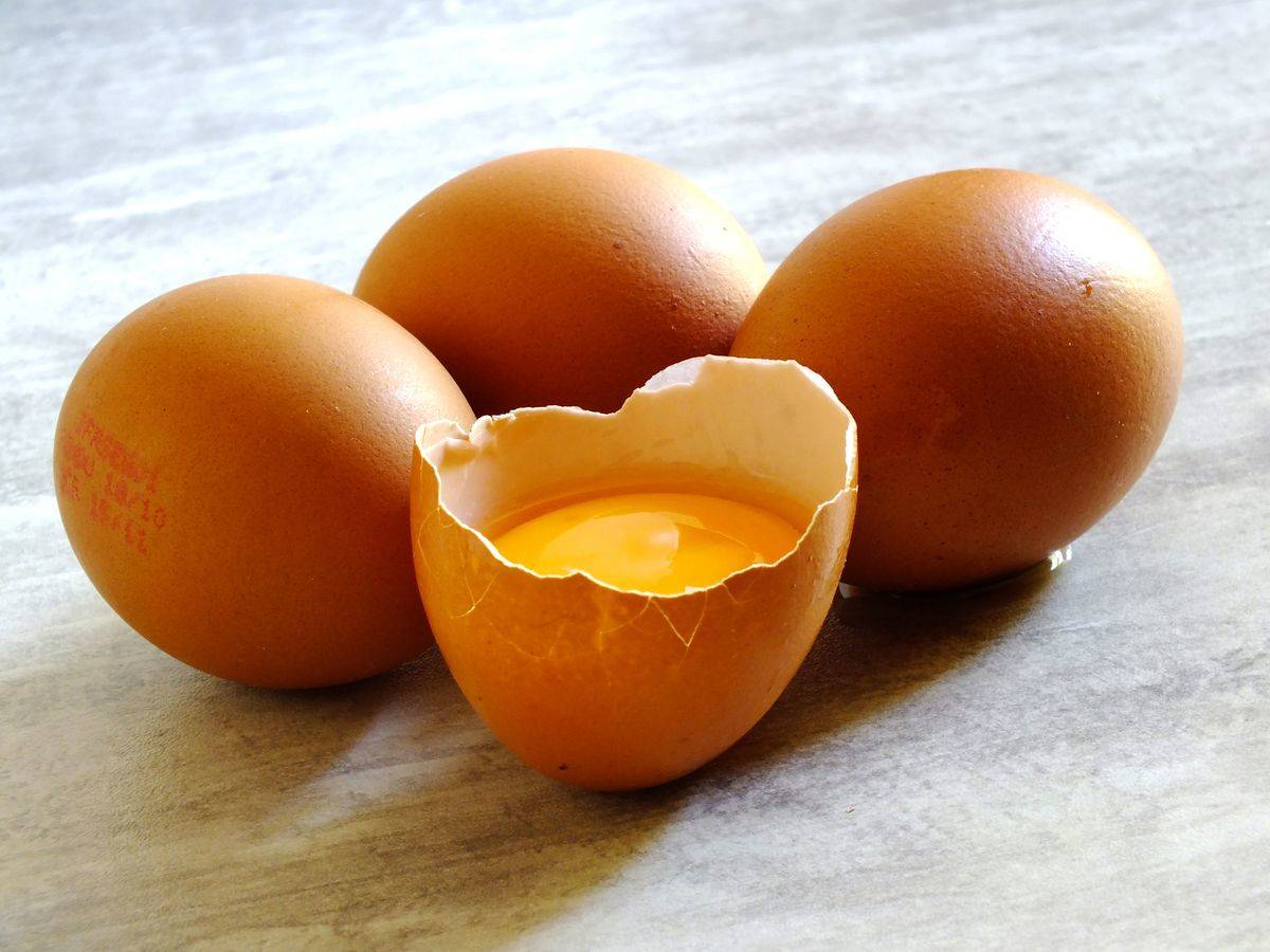 Four brown eggs site on a table; one is broken open.