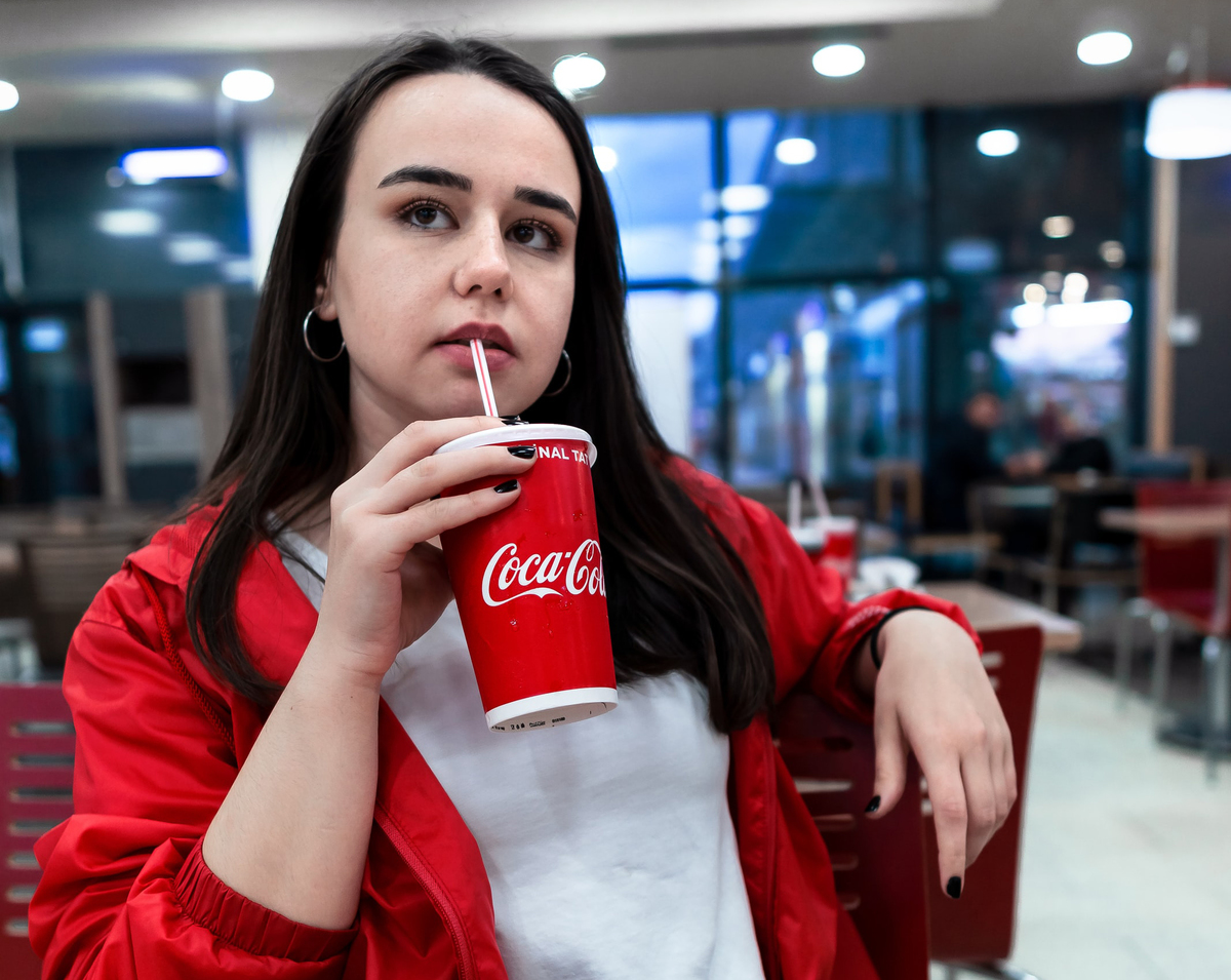 A woman drinks soda in a cafeteria.