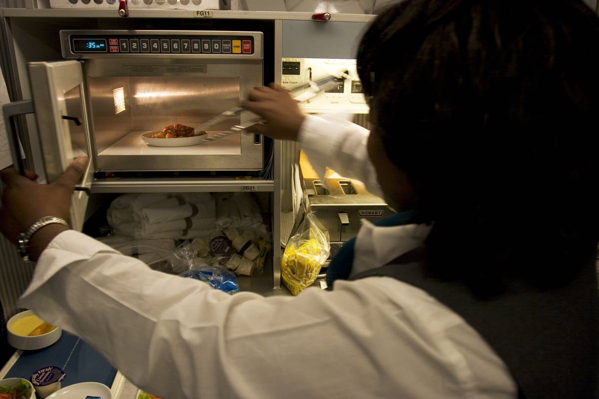 A woman takes leftovers out of a microwave.