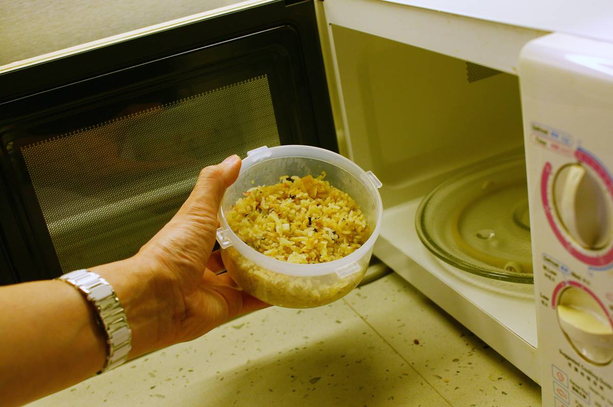 A woman puts a container of leftover rice into the microwave.