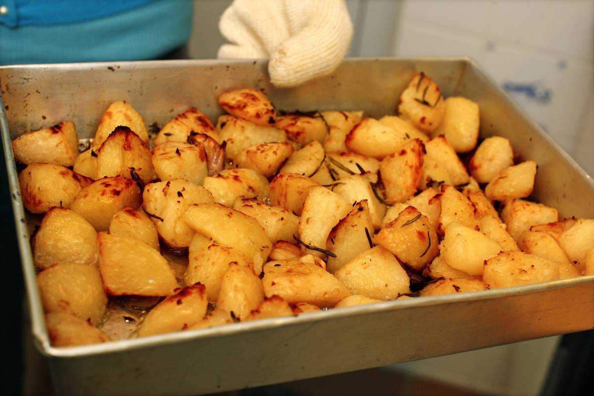 A chef holds a pan of roasted potatoes.