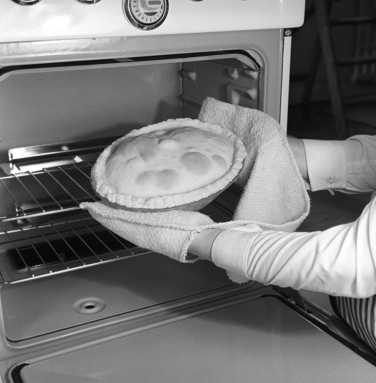 A woman takes a pie out of the oven with pot holders.
