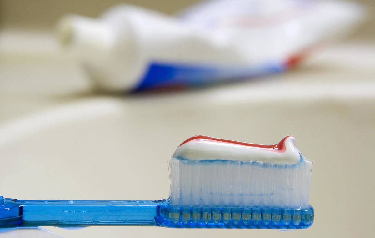 A toothbrush is pictured with toothpaste on it in front of a sink.