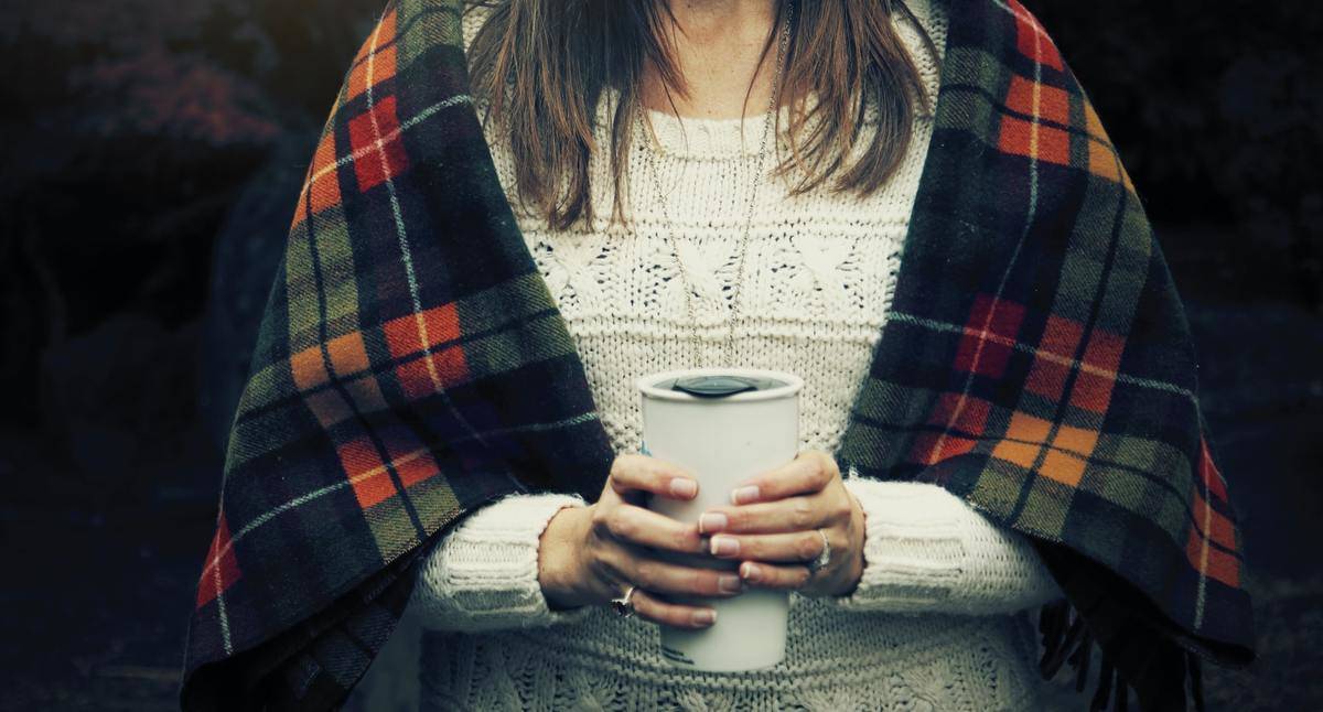 A woman holds a white travel mug.