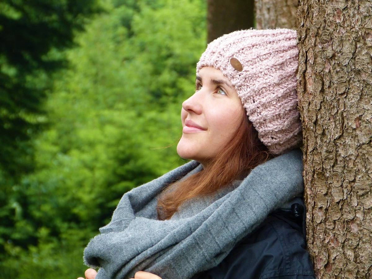 A woman leans against a tree and smiles as he thinks.